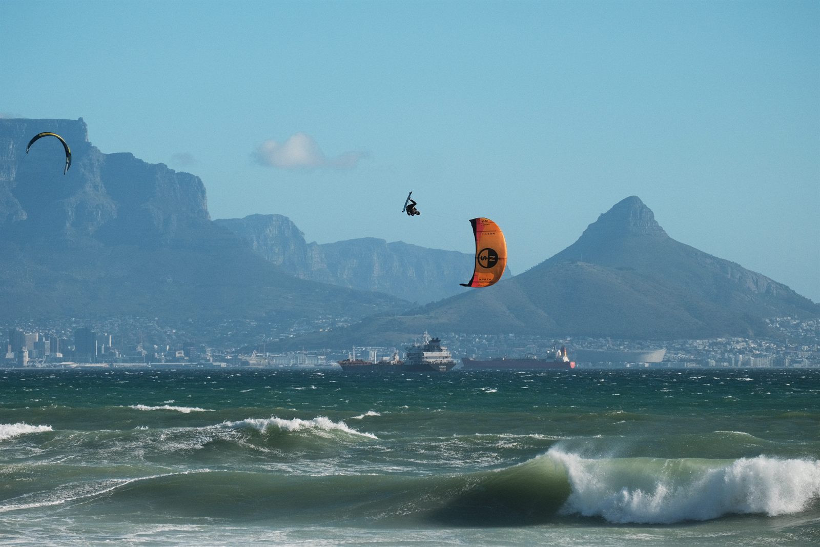 A kitesurfer boosting big air over Table Bay, with Table Mountain and Lion's Head across the water from Bloubergstrand